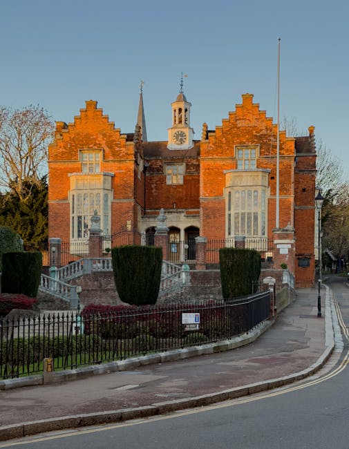 A residential street scene taken during sunset, featuring clean, well-maintained white and brick buildings with modern design, large windows, and balconies. The asphalt road has clear white markings, including a 'KEEP CLEAR' notice, and the pavement is composed of small, interlocking bricks. The street is illuminated by natural light from the setting sun, casting warm hues across the scene, with no visible litter or debris, indicating regular cleaning and maintenance. This image represents an urban environment in Harrow, suitable for illustrating a professional domestic or commercial cleaning service such as that provided by Cleaner Harrow at the end of tenancy or surface cleaning for flats on Station Road.